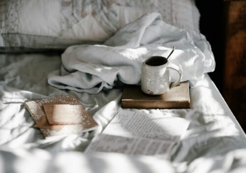 Notebook with journal prompts on a bed next to a warm beverage