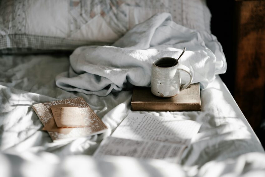 Notebook with journal prompts on a bed next to a warm beverage