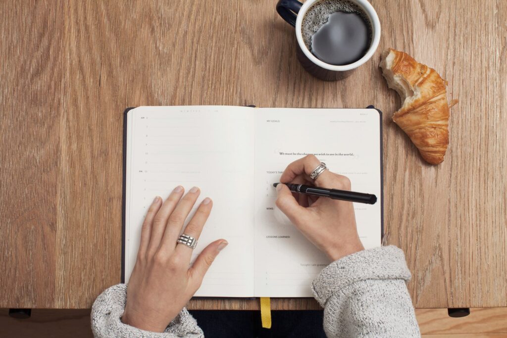 Lady answering Christmas journal prompts in her diary while having coffee and a croissant