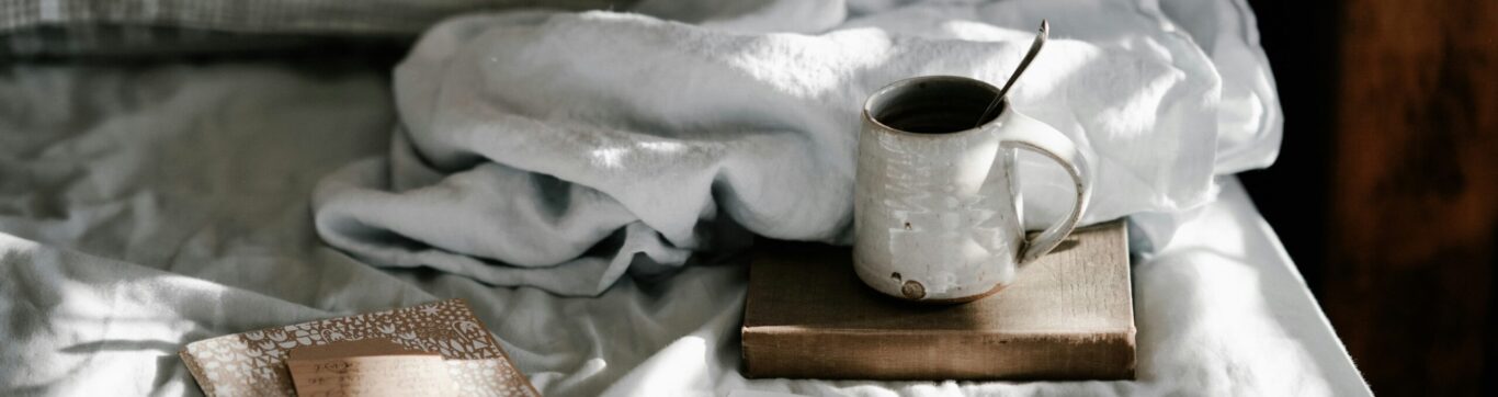 Notebook with journal prompts on a bed next to a warm beverage